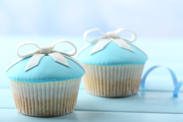Tasty cupcake with bow on color wooden table, on bright background