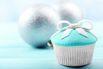 Tasty cupcake with bow and Christmas toys on color wooden background