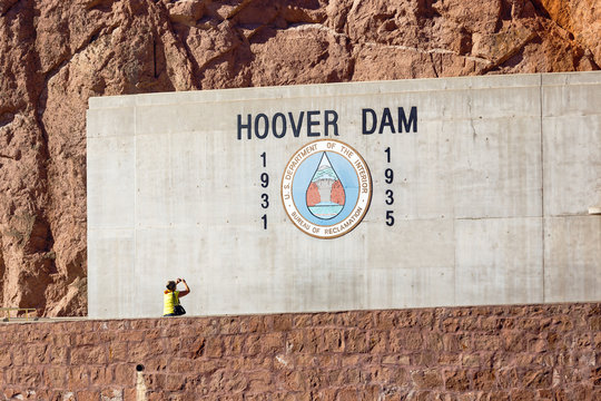 Woman taking pictures of hoover dam logo. Woman photographed sign logo at entrance to Hoover Dam on the concrete wall on red rocks bakground.