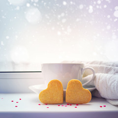 Two heart-cookie, cup of coffee and a blanket against a snowy ba