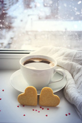 Cup of coffee and two cookies in the shape of a heart against th