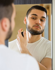 Young guy using perfume at home.