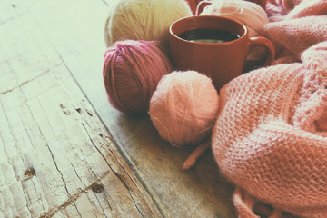 selective focus photo of pink cozy knitted scarf with to cup of coffee and wool yarn balls on a...