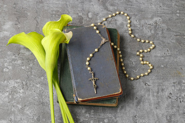 White calla flowers (Zantedeschia), rosary and Holy Bible on sto