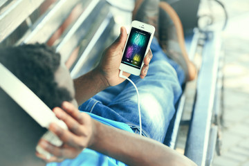 African American man listening music with headphones on bench in park