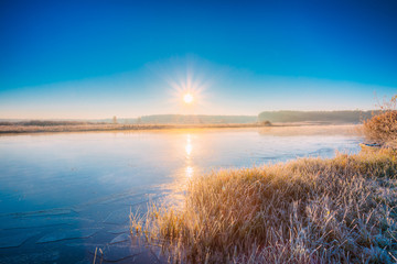 Sun rises over the river. Autumn frost frozen river covered with