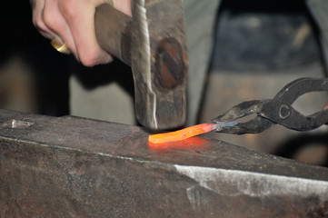 Detail shot of hammer forging hot iron at anvil