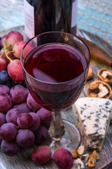 Red wine bottle, grapes, walnuts and cheese on a wooden background