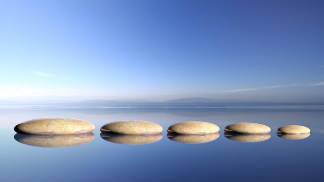 Zen stones row from large to small  in water with blue sky and peaceful landscape background