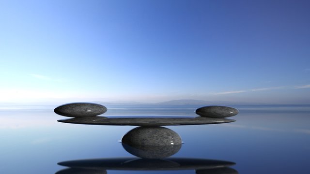 Balancing Zen stones in water with blue sky and peaceful landscape.