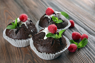 Delicious chocolate cupcakes with berries and fresh mint on wooden table close up