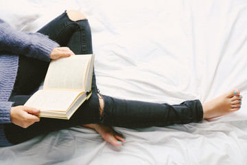 Obraz premium Woman in black jeans reading book on bed top view point