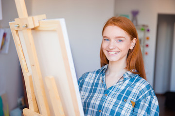 Pretty cheerful young woman painter painting in art studio