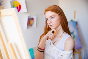 Thoughtful pretty young redhead woman artist thinking and making sketches