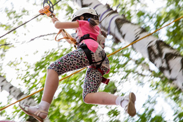 Naklejka na ściany i meble brave girl moves on zipline in adventure park..