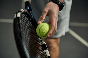 Tuinposter Close-up of male hand holding tennis ball and racket. Professional tennis player starting set.  © Stasique