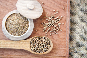 coriander seeds in a wooden spoon, milled in bowl.