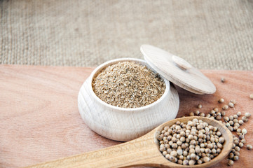 coriander seeds in a wooden spoon, milled in bowl.