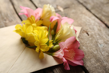 Fresh bouquet of flowers in envelope on wooden background