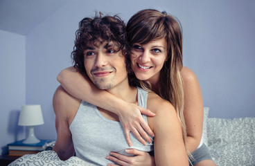 Couple in love embracing and smiling sitting over bed