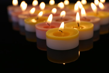 Many burning small candles on dark background, close-up