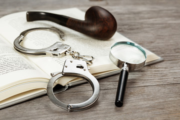 handcuffs, magnifying glass and pipe on book