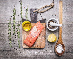 salmon fillets with oil, lemon, salt and pepper, herbs on a cutting board  on wooden rustic background top view close up