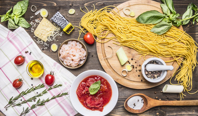 Ingredients for cooking pasta, tomatoes in own juice, basil, shrimp, grater, cherry tomatoes, wooden spoon, chopping board on wooden rustic background top view