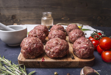 raw meatballs on a cutting board with vegetables and herbs on wooden rustic background  close up