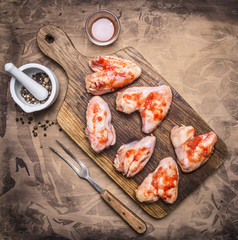 raw chicken wings with barbecue sauce and pepper, fork for meat on a cutting board on wooden rustic background top view close up