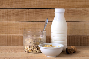 Muesli. Milk in the bottle and muesli in white plate and a glass jar on a wooden background.
 