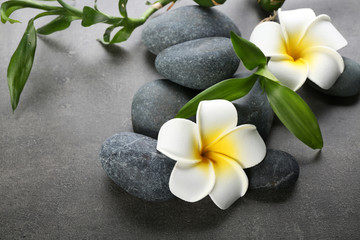 Fototapeta na wymiar Hot spa stones with flowers and bamboo on grey background, close-up