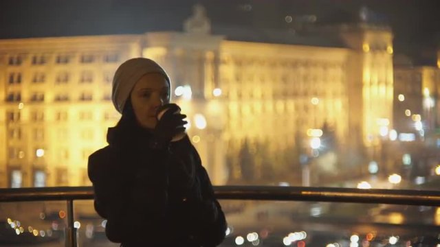 Woman on the street of the evening drinking coffee and talking on the phone