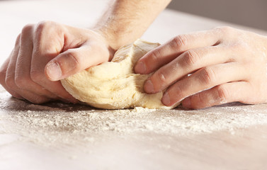 Hands kneading dough for pizza on the wooden table, close-up