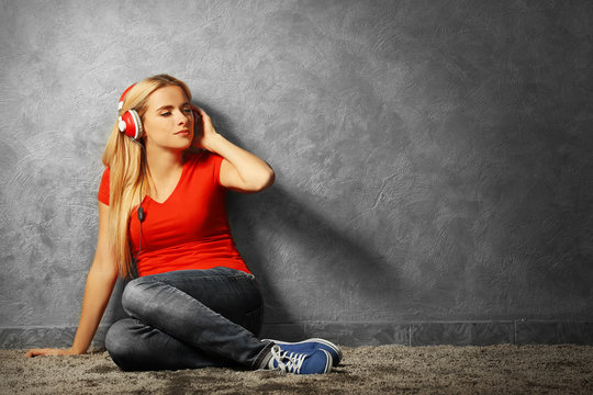 Young woman sitting on the floor and listening to music on a grey wall background