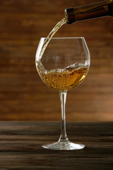 White wine pouring in glass on wooden background