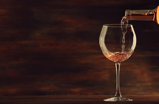Rose wine pouring in glass on wooden background