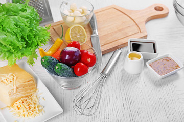 Kitchen utensils and ingredients for salad on table, on light background