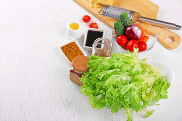 Kitchen utensils and ingredients for salad on table, on light background