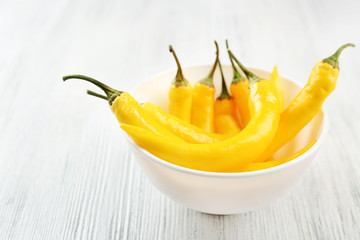 Yellow chili peppers in bowl, on light wooden background