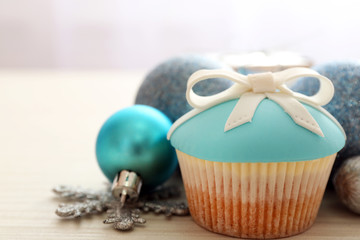 Tasty cupcake with bow and Christmas toys on color wooden background