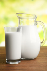 Milk in jar and in glass on table on blurred natural background