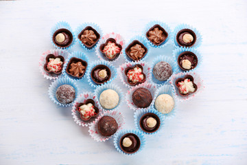 Set of chocolate candies forming heart on a light wooden background