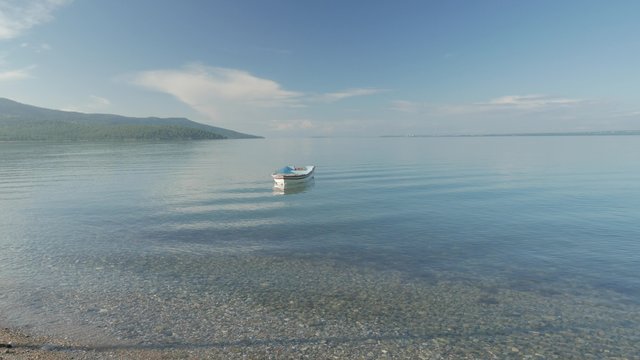 Lonely row boat floating on clear water with small waves in the morning. 4k