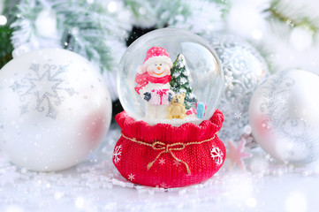 Fototapeta na wymiar A snow globe with snowman on background spruce branches with sno