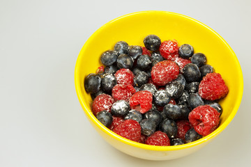 Frosted raspberries and blueberries in a bowl, isolated on white