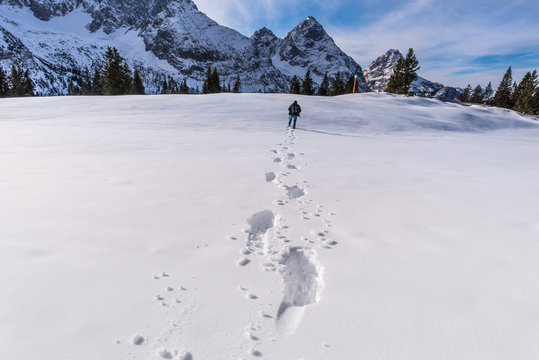 Winter scenery with a man walking through snow on a mountain peak, leaving a trail of footsteps behind him. Picture taken on Austrian Alps, near Ehrwald resort. 
