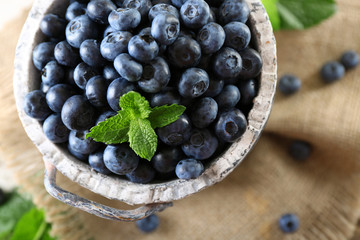 Tasty ripe blueberries with green leaves in bucket on table close up