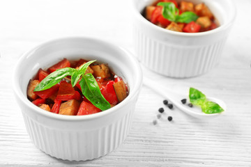 Tasty vegetarian ratatouille made of eggplants, squash, tomatoes in bowls on wooden table background