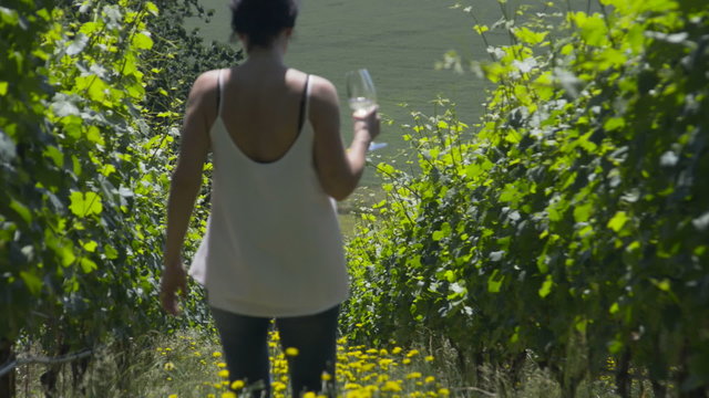 Woman walks down Vineyard row to a man while holding a glass of wine